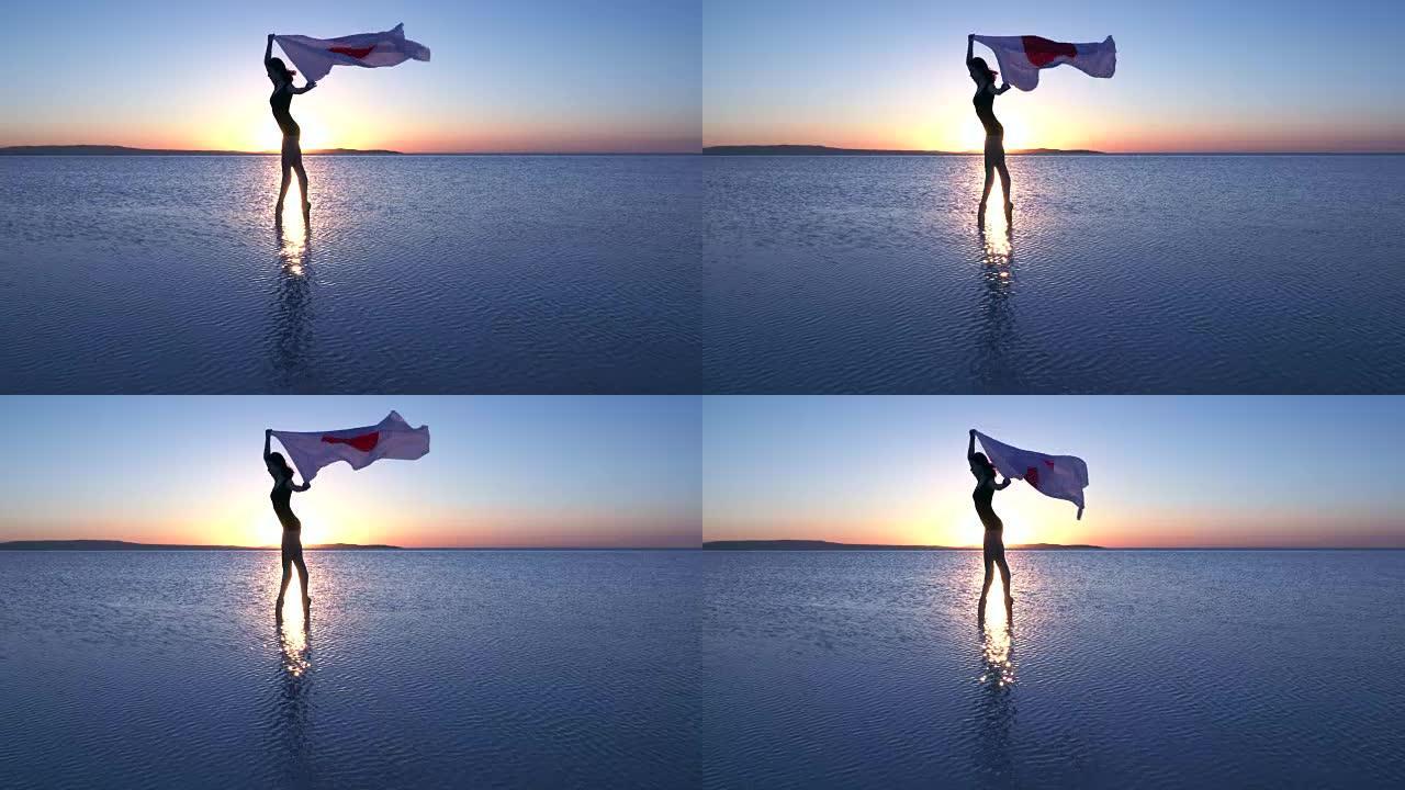 美丽的芭蕾舞演员在水上举着一面日本国旗。有风的一天。