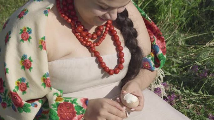 穿着传统衣服的白人超重妇女的肖像坐在草地上清洗鸡蛋。