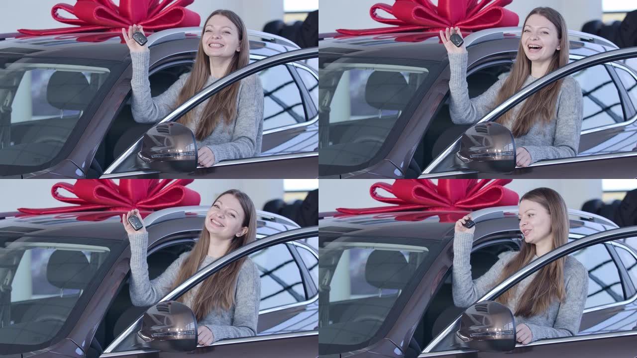 年轻的白人妇女站在汽车经销店的新车上，带着钥匙和微笑。在陈列室里，快乐的女主人在车辆旁边摆姿势。电影