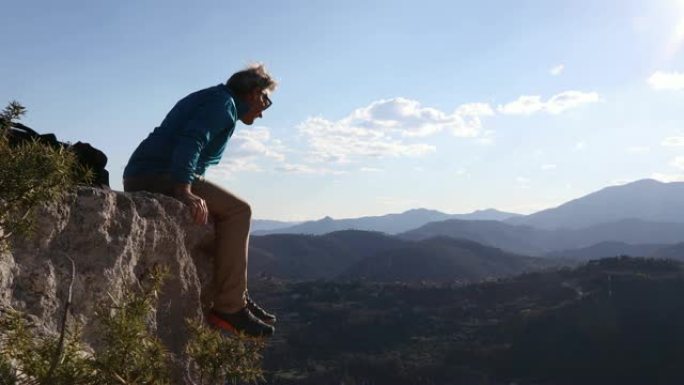 男性徒步旅行者到达山谷上方的岩石顶，山脉