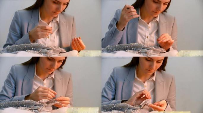 一位年轻的女孩设计师在工作室服装中缝制了一件衣服。做衣服缝制珠子和珠宝。女裁缝在工作室装饰一件衣服