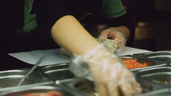 戴着一次性手套的炊具将鸡蛋放入自己动手的面包卷中，从玻璃冰箱中取出配料
