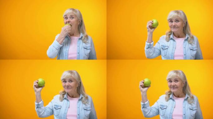 乐观的老年女士咬着新鲜的青苹果，健康的牙齿，口腔医学