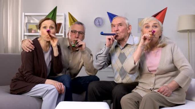 欢快的老年人戴着生日帽子吹着派对喇叭，庆祝，派对
