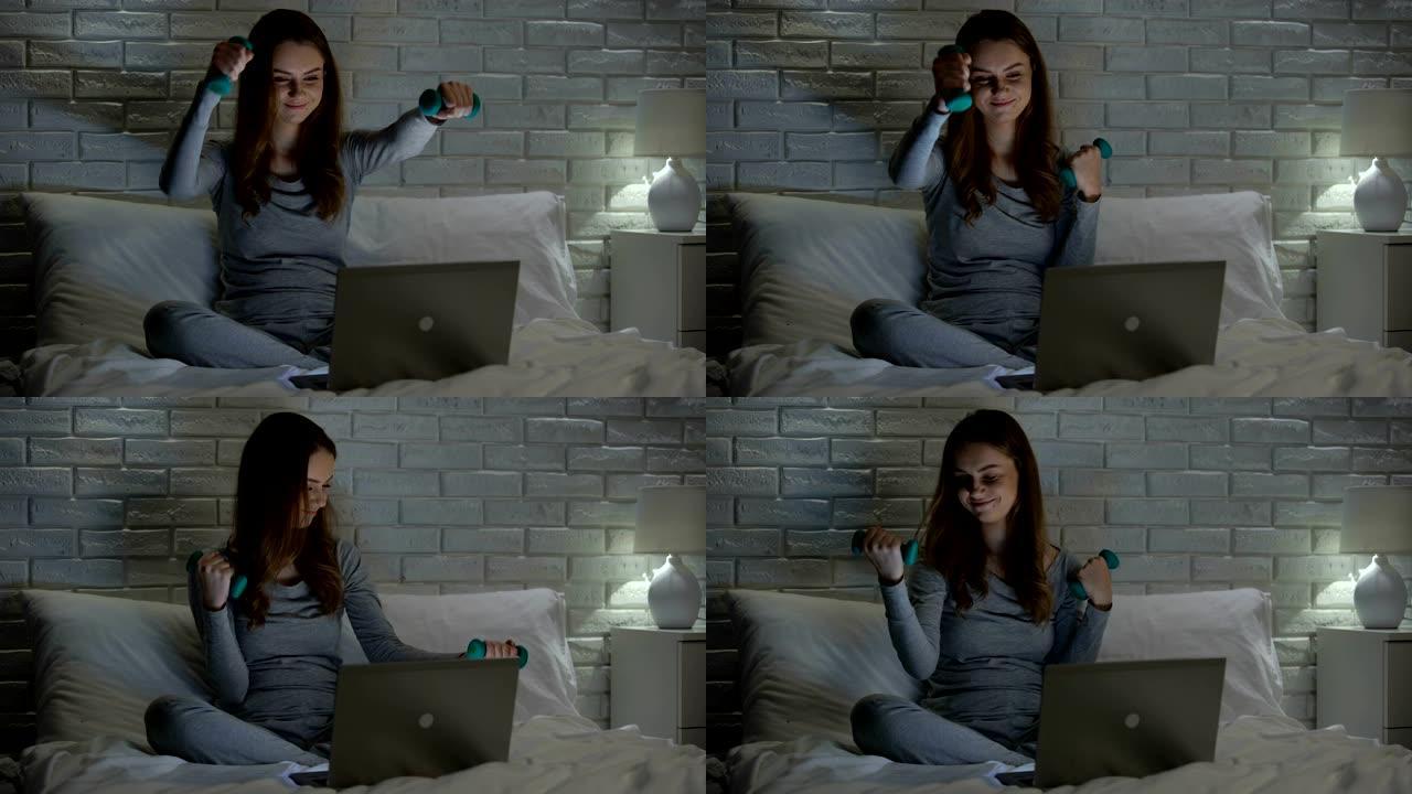 懒惰的女孩在床上举起哑铃观看网络减肥教程