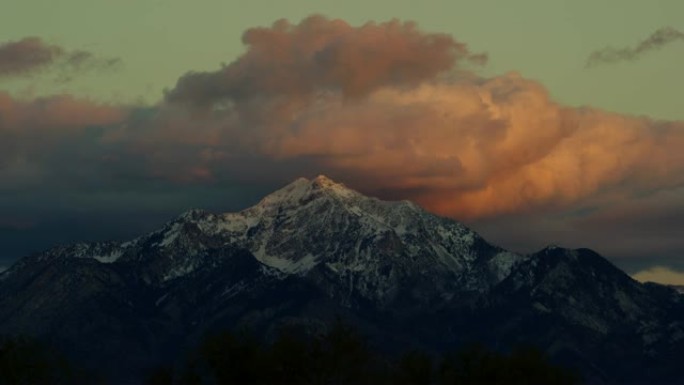 犹他州盐湖城上空白雪皑皑的瓦萨奇山脉在日出/日落时的时间流逝，带有戏剧性的云景