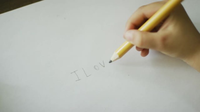 一名白人五岁孩子的手在纸上用铅笔写下 “我爱妈妈”