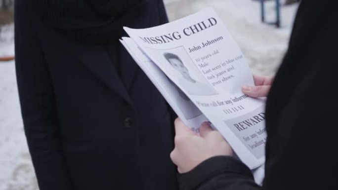 年轻的白人男子在街上向无法辨认的女人发出失踪的儿童广告。父亲在寻找被绑架的儿子。失落，沮丧，绝望。