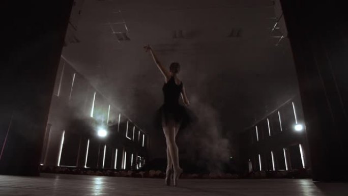 在聚光灯前慢慢跳舞的芭蕾舞演员。几个聚光灯显示了一个慢动作在黑暗舞台上跳舞的芭蕾舞演员。