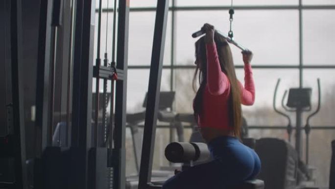 女孩在健身房锻炼时摇着背。在带有大窗户的房间里训练一个女人使用椭球和跑步机