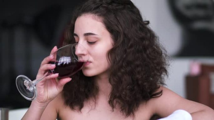 棕色眼睛的黑发女人在洗澡时喝葡萄酒的肖像。年轻美丽的白人女孩享受酒精休息在浴室在家里或酒店。