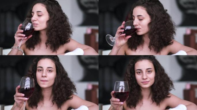棕色眼睛的黑发女人在洗澡时喝葡萄酒的肖像。年轻美丽的白人女孩享受酒精休息在浴室在家里或酒店。