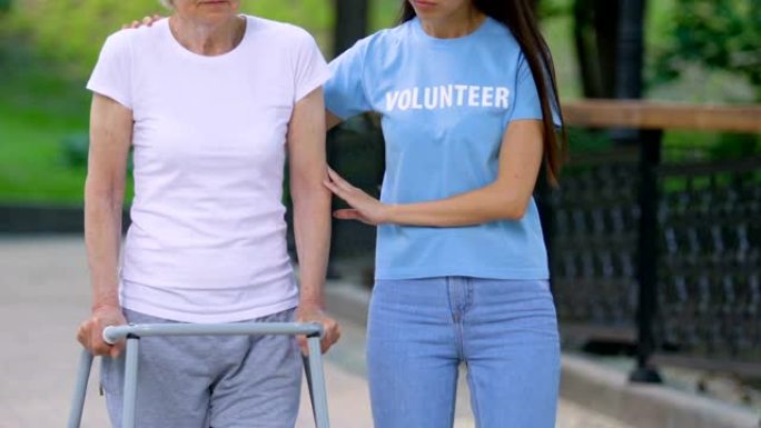 志愿者在医院公园里用步行架支持老残疾妇女
