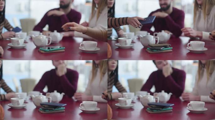一群无法识别的人的特写镜头，将智能手机放在咖啡馆的桌子上。朋友聚集在餐厅里度过没有设备的时光。现代社