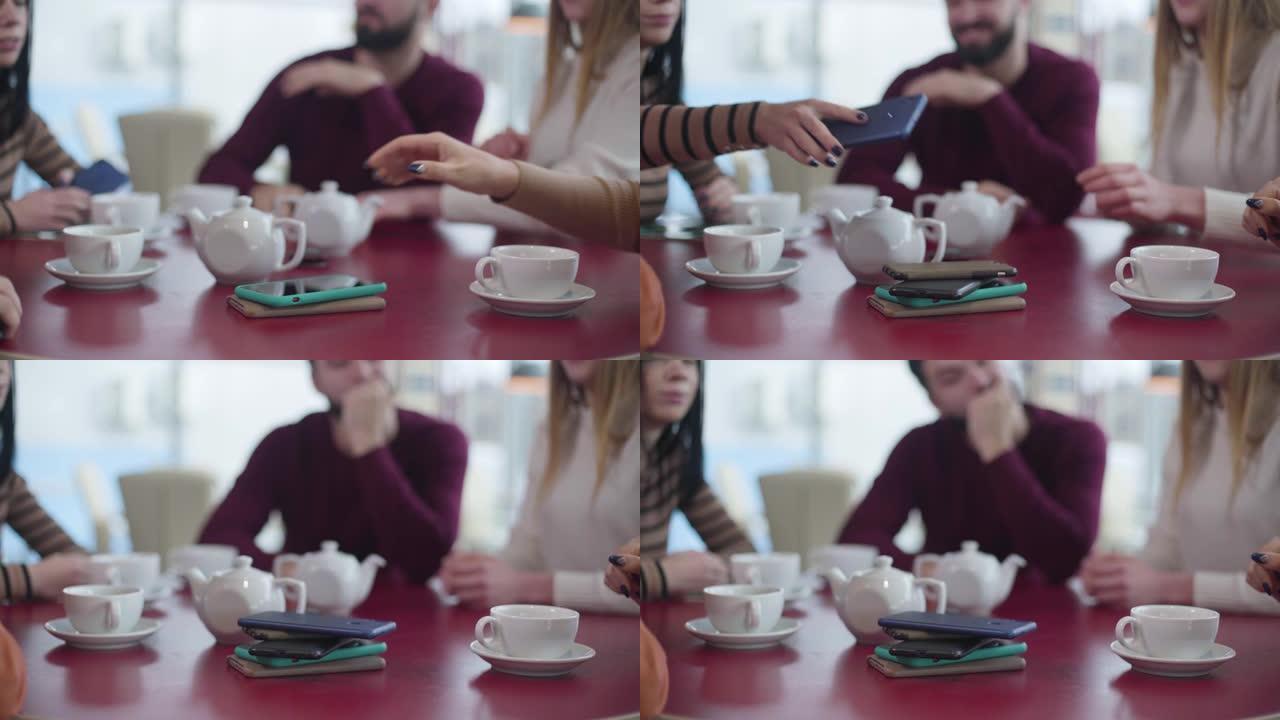 一群无法识别的人的特写镜头，将智能手机放在咖啡馆的桌子上。朋友聚集在餐厅里度过没有设备的时光。现代社