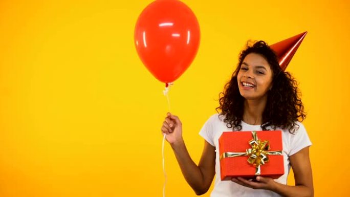 开朗的混血儿女孩拿着礼品盒和气球，庆祝生日派对