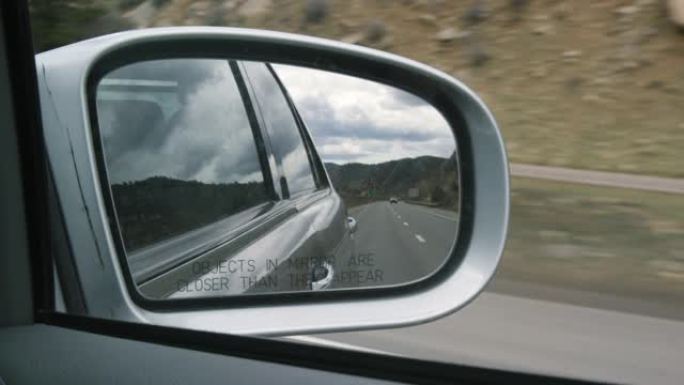 70号州际公路，汽车，科罗拉多州的落基山脉，以及在汽车侧面后视镜中反射的多云天空 (镜子中的物体比它