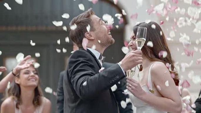 SLO MO新婚夫妇在玫瑰花瓣淋浴中敬酒和亲吻