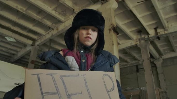 一个穿着脏衣服的无家可归的高加索女孩举起帮助纸板并看着相机的仰视图