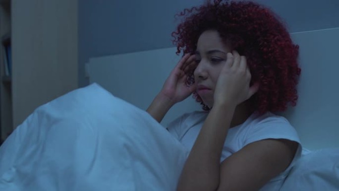 年轻女子感到头痛，晚上坐在床上，按摩太阳穴，健康