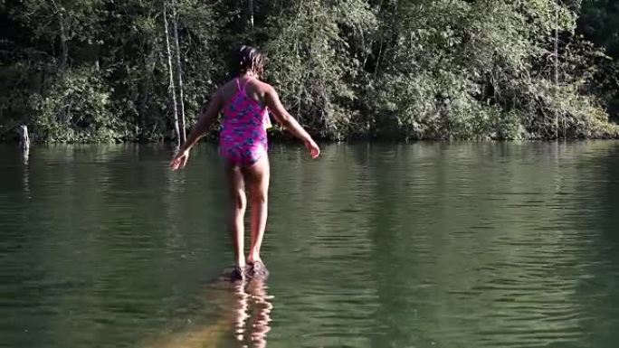 年轻的混血女孩在湖边沉没的原木上保持平衡