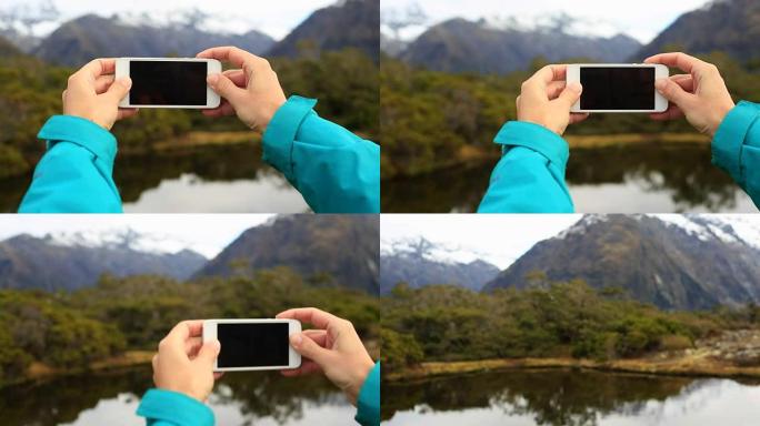 女人徒步旅行并拍摄智能手机照片的个人视角山湖景观