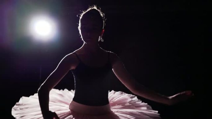 专业芭蕾舞演员在工作室的黑色背景下，在她的脚尖芭蕾舞鞋上跳舞。芭蕾舞演员展示了穿着芭蕾舞短裙和尖头鞋
