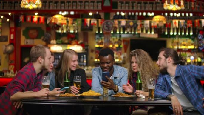 非裔美国人在手机上给朋友看照片，他们坐在酒吧里慢动作时看着笑。青年男女公司