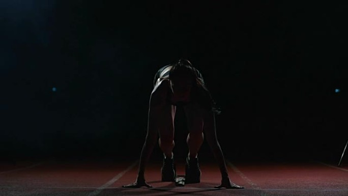 穿着黑色短裤和t恤的年轻女运动员正准备在起跑线附近的跑步机上开始100米比赛