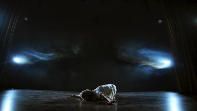 穿着白色连衣裙的现代舞女人在舞台上跳现代芭蕾舞，跳，在蓝色聚光灯下用烟雾旋转。