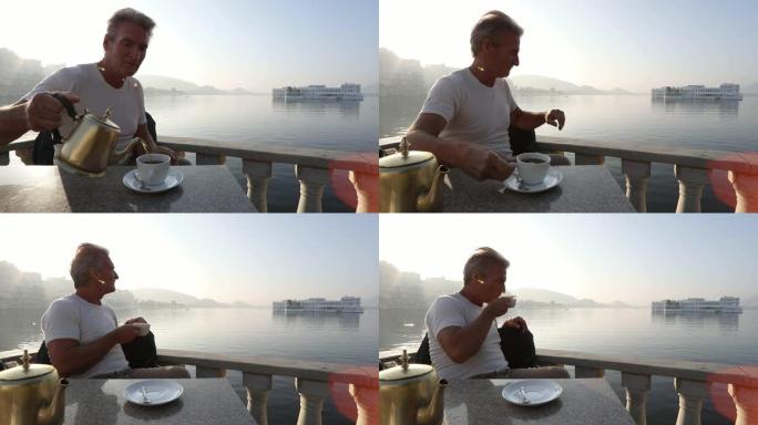 男人在日出时在湖岸上倒茶