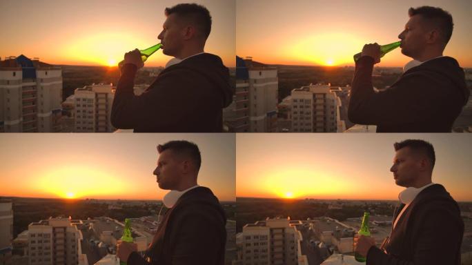 一个男人站在屋顶上喝着啤酒，沉思着世界。从高处看这座城市日落时的景色。摩天大楼的屋顶