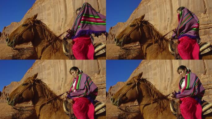 在晴朗明亮的日子里，一个十几岁的美国印第安女孩在亚利桑那州/犹他州纪念碑谷沙漠骑马时，在肩膀上披上五