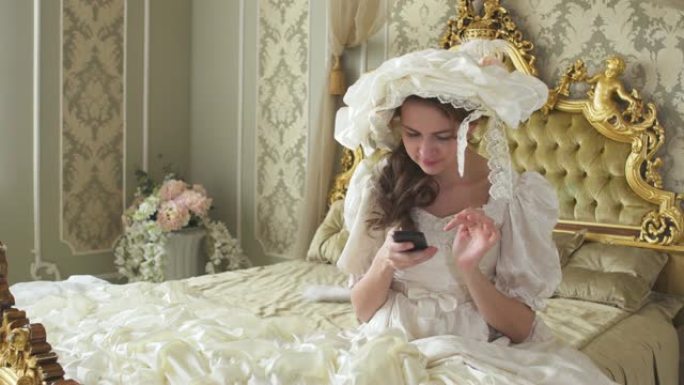 穿着舞会礼服的年轻女子坐在金色装饰的床上，用手机发短信。公主使用小工具