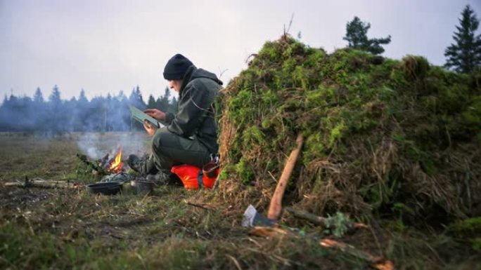 DS男子坐在篝火旁，在大自然中读书