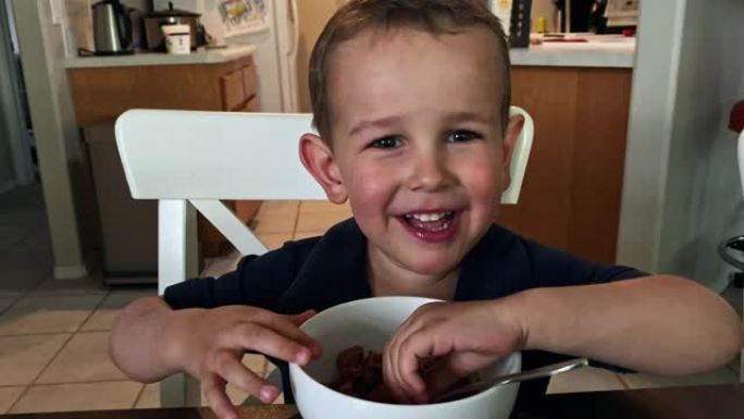 一个可爱的四岁白人男孩在家庭厨房用餐时用手捡起食物时笑着笑