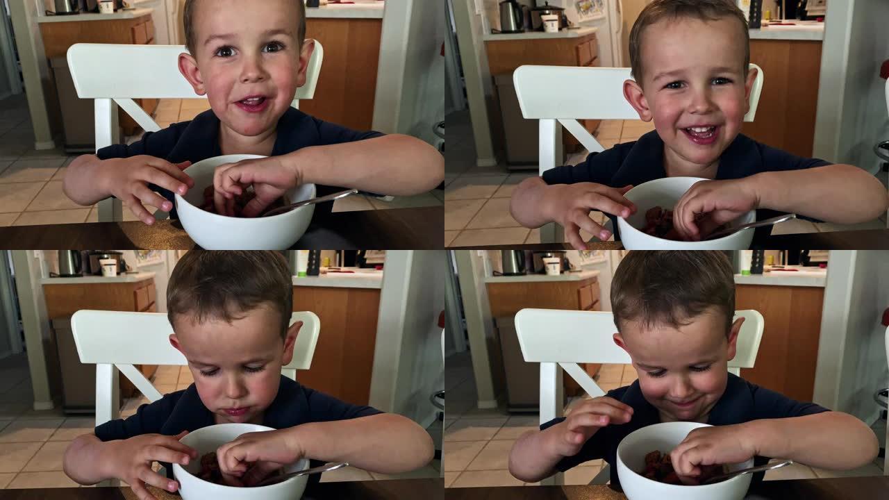 一个可爱的四岁白人男孩在家庭厨房用餐时用手捡起食物时笑着笑