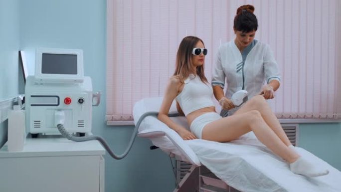 穿着白色浴袍的年轻女子在美容师诊所进行激光脱毛手术，慢动作。医生去除病人腿部或身体的毛发。概念。