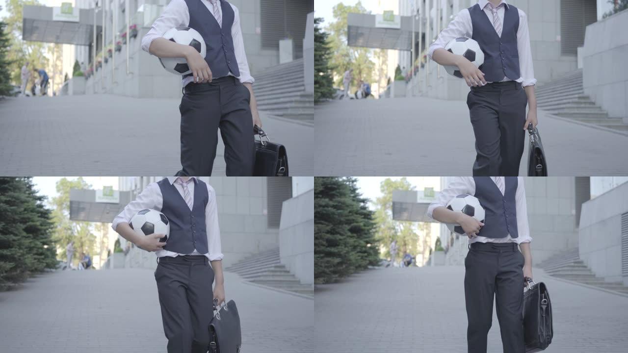 可爱的男孩走在街上，手里拿着足球和钱包。