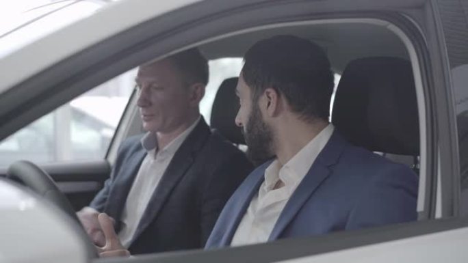 富裕的中东人与汽车经销商交谈的侧视图。成功人士在经销商处选择车辆的特写镜头。陈列室的交易员咨询客户。