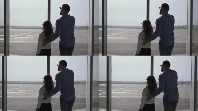高加索男子和小女孩的轮廓的后视图，从跑道的玻璃机场门口望去。父女手握在额头上。等待飞机起飞的家庭。
