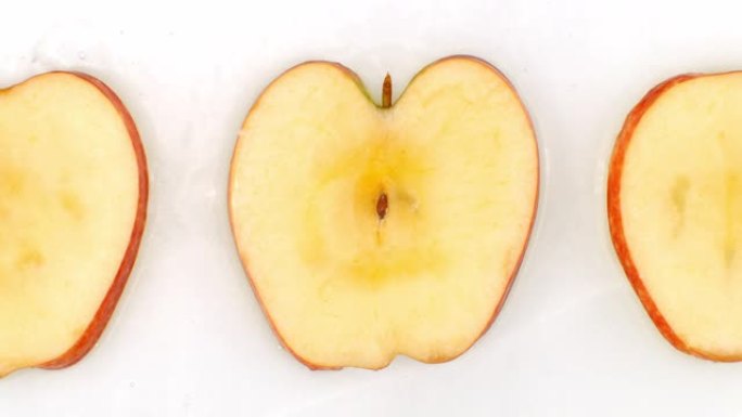 水以慢动作飞溅。俯视图: 在白色背景上用水洗净的三片甜苹果。