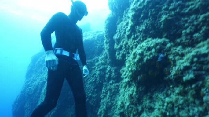 水肺潜水员触摸礁石并浮出水面的水下视图