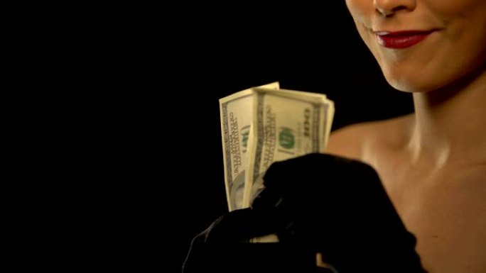 微笑的女士向相机展示一束美元，孤立在黑色背景上