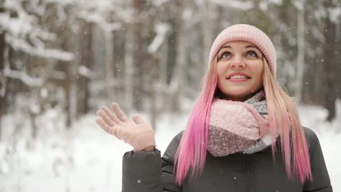 慢动作，冬天的女人在树林里看着雪落下，微笑着看着天空，直接对着镜头