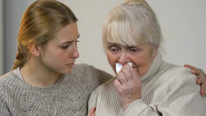 年轻的女士安慰不幸哭泣的奶奶遭受损失，在家庭中得到支持