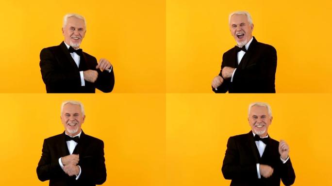 快乐英俊的养老金领取者在橙色背景上跳舞，在相机上微笑，有趣