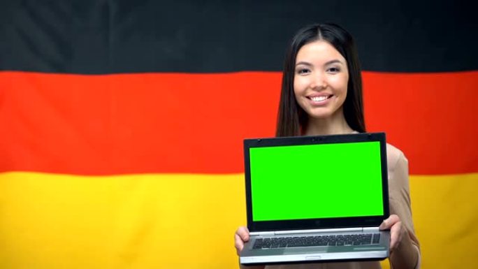 女孩拿着带绿屏的笔记本电脑，背景是德国国旗，旅行