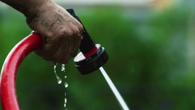 一名高加索人的手在他的住宅后院使用连接到软管上的喷嘴来浇水