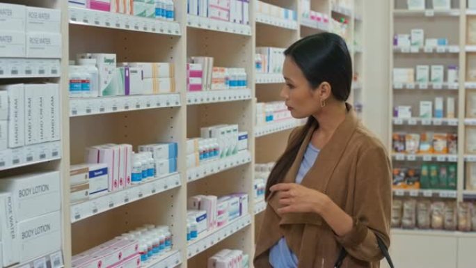 DS亚洲妇女站在药房的架子上，并阅读药瓶背面的标签